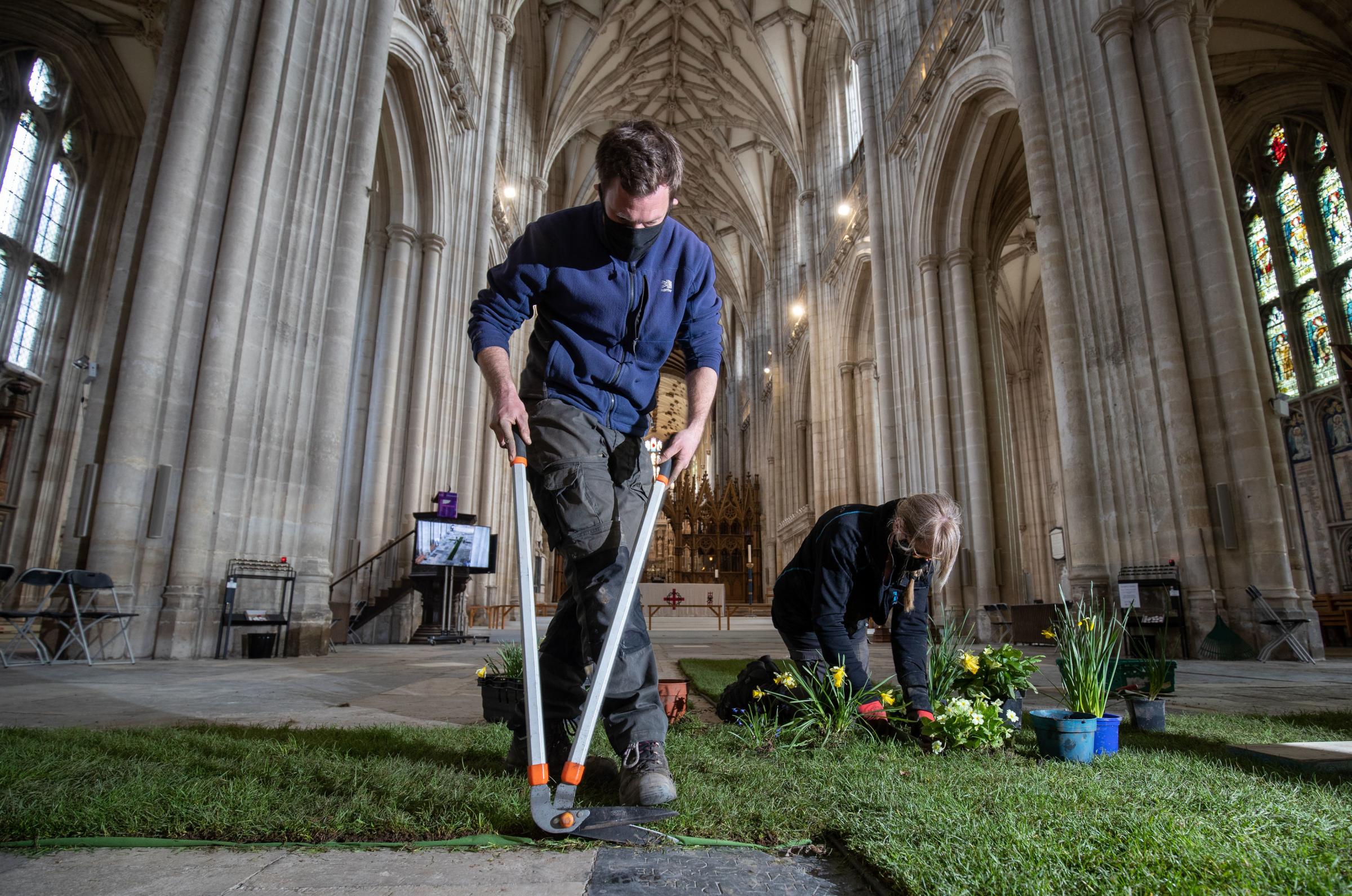 EMBARGOED TO 0001 TUESDAY MARCH 23 Gardeners work on a green meadow cross, which is to be adorned with daffodils and spring flowers and surrounded by candles, in the Nave of Winchester Cathedral, ahead of the National Day of Reflection to remember those